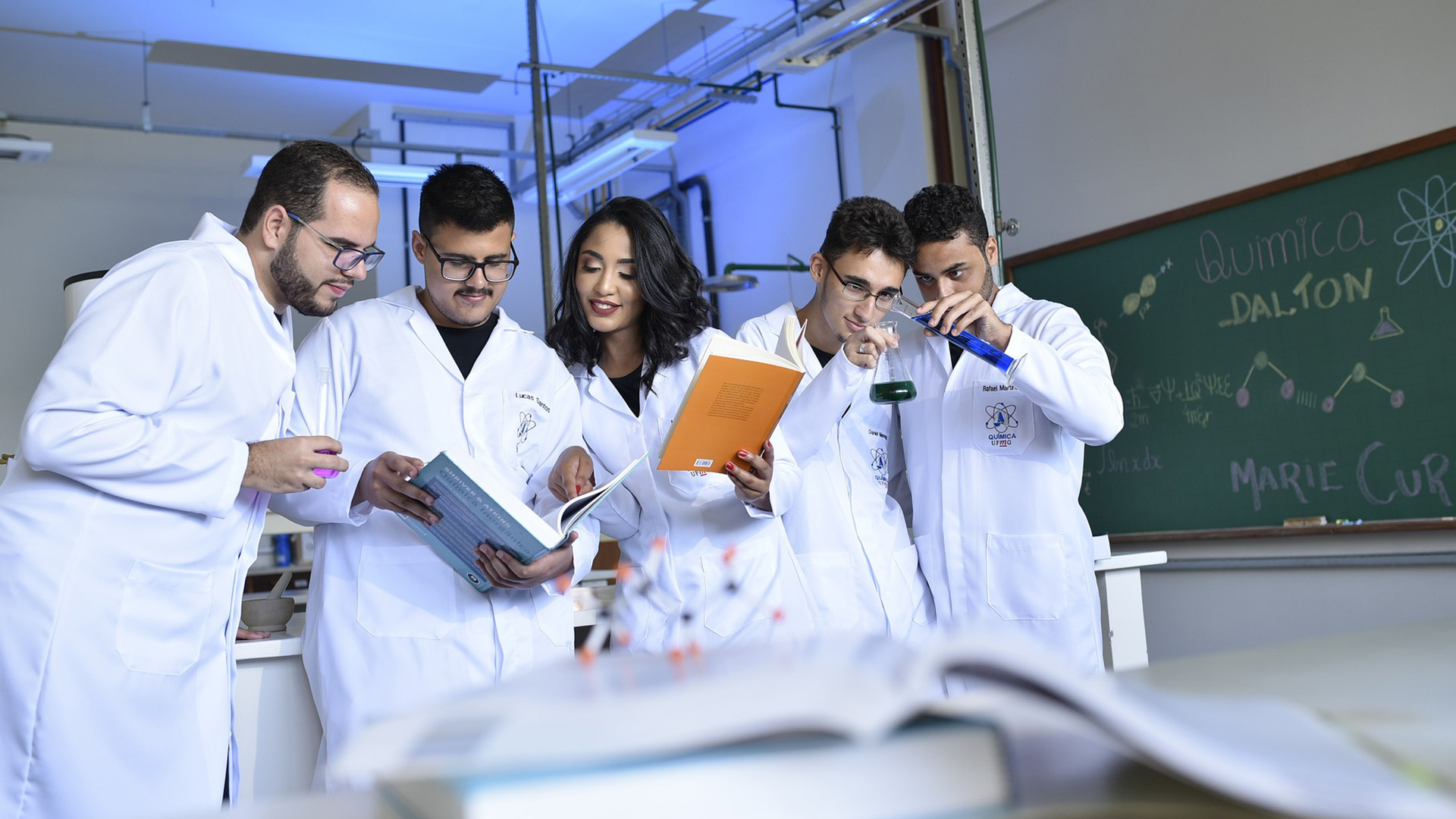 Wissenschaftler und Wissenschaftlerinnen in weißen Kitteln, die in Büchern lesen und miteinander sprechen.